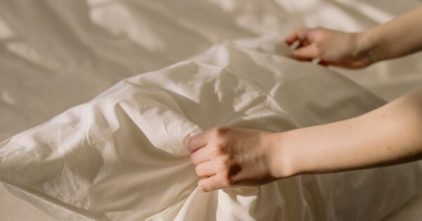 A close-up of hands adjusting a pillow on a neatly made bed, bathed in warm sunlight.